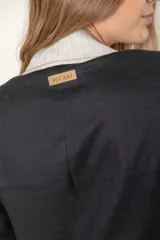 Blazer de lino color blanco con solapas y cuello en color beige, corte entallado, botón de nácar, tajo en la espalda y bolsillos laterales.