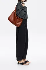 Bolso de mano negro con exterior de piel y estructura blanda. Incluye asa extraíble, bolsillo interior y etiqueta de tejido. Presenta logo metálico BIMBA Y LOLA con acabados metálicos plateados.