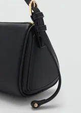 Bolso negro tipo baguette con correa de hombro fina y charm dorado en forma de esfera.