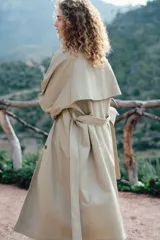 Gabardina midi color beige de algodón, con doble botonadura, cuello con solapas, cierre de corchete en la parte superior, solapa de tormenta en la espalda, bolsillos laterales con solapa, cinturón extraíble con hebilla rectangular, mangas raglán con trabilla ajustable en los puños y abertura trasera.
