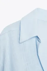 Camisa blanca de cuello solapa y manga larga con puños. Tiene un nudo en la parte delantera y cierre frontal con botones.