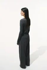 Pantalón negro de sarga suave con cintura elástica, cordón de ajuste en color contrastante y franjas laterales finas. Modelo de corte holgado con tiro alto, bolsillos laterales discretos y bolsillos insertados decorativos atrás. Piernas amplias con pliegues adelante y atrás.