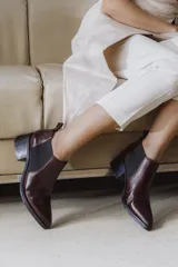 Botín negro de cuero vacuno con acabado charol, estilo botín Chelsea con puntera fina y elástico lateral. Posee un taco ancho y bajo de 5.5 cm.