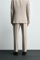 Pantalón de vestir color beige, corte slim fit, confeccionado en tejido con viscosa. Cuenta con bolsillos frontales y traseros de doble vivo con botón. Cierre frontal con cremallera y botón.