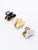 Set de tres pinzas para el pelo tipo clip, con cuerpo dorado y superficie en negro con glitter, amarillo con glitter y blanco con glitter.