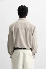 Camisa color crema de corte relaxed fit, confeccionada en tejido de mezcla de algodón suave al tacto. Tiene cuello solapa, manga larga con puños abotonados, un bolsillo de parche en el pecho y cierre frontal con botones.