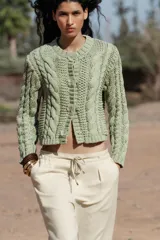 Chaqueta de punto color verde claro, con cuello redondo y manga larga. Cierre frontal con botones a presión en forma de flor.