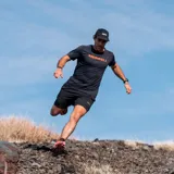 Remera deportiva naranja de poliéster y spandex, con logo Merrell estampado en el pecho.