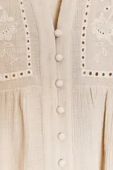 Blusa blanca de cuello solapa y manga larga abullonada terminada en volantes. Presenta bordados florales calados en el frente y cierre frontal con botones.