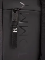 Bandolera negra de poliuretano con correa ajustable, cierre de cremallera, bolsillo exterior con cremallera, logo tonal de Tommy Jeans y parche engomado de Tommy en la parte delantera.