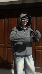 Campera con capucha y cierre frontal, color hueso con rayas finas horizontales en tono oscuro. Presenta un calce holgado (boxy fit) y puños y cintura acanalados.