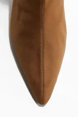 Botines de caña elástica entallada, color marrón, con punta fina y taco bajo forrado. Presentan costura frontal y cierre lateral.