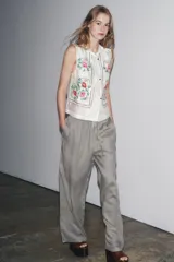 Top blanco de cuello mao y sin mangas, con bordados florales en el frente y cierre con botones.