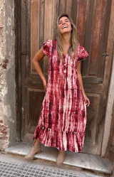 Vestido largo de seda con estampado tie-dye en tonos rojo y blanco, con mangas cortas con volados y ruedo con volados.