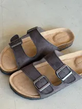 Sandalias de cuero sintético color marrón con doble tira y hebillas metálicas ajustables.