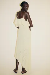 Vestido midi color crema confeccionado en encaje, con escote recto, tirantes finos, volantes y tachas.