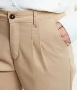 Pantalón de jean color beige, corte mom, con trabillas en la cintura, pliegues delanteros, cierre tradicional y bajo con dobladillo.