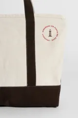 Bolso tipo totebag de lona color crudo con base y asas en color rojo. Estampado frontal con el texto "The Beach Club" en rojo.