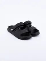Sandalia tipo 'slide' de goma, color negro, con dos tiras anchas y acolchadas sobre el empeine, ajustables mediante un broche blanco en el lateral.