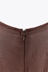 Vestido midi color marrón con textura brillante y arrugada, cuello redondo y mangas cortas tipo murciélago. Presenta un canesú fruncido con pliegues verticales en la cintura que da paso a una falda de corte A.