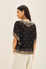 Blusa de gasa traslúcida negra con escote en V y mangas amplias de largo irregular, bordada con canutillos, lentejuelas y mostacillas doradas. Incluye gancho oculto en el escote y viso al tono con breteles regulables y puntilla en el escote.