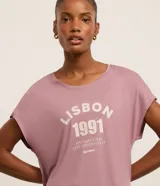 Remera deportiva de modal color lila con cuello redondo y mangas cortas. Estampa frontal con la leyenda "Lisbon 1991. Live like your life depends on it. Europe".