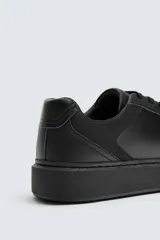 Zapatilla urbana de cuero sintético color negro, con cordones y suela de plataforma.