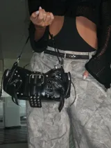 Cartera bandolera negra con múltiples hebillas, tachas y cierres.