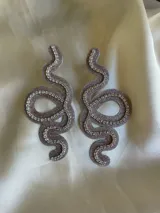 Par de aros colgantes con forma de serpiente contorneada en strass y cierre a presión de acero inoxidable.