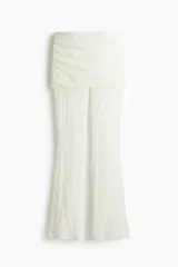 Pantalón largo de encaje blanco con corte acampanado y falda mini superpuesta con laterales fruncidos y cintura elástica.