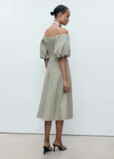 Vestido midi verde oliva de lino, con escote off-shoulder y mangas cortas abullonadas. Tiene corte evasé y cierre de cremallera en la espalda.