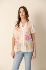 Camisa de seda blanca con bordados florales multicolores, cuello camisero, manga corta y cierre frontal con botones forrados.