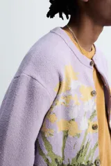 Cárdigan lila con diseño floral, cuello redondo, manga larga, rib en puños y ruedo, y cierre frontal con botones.