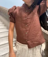 Camisa color ladrillo confeccionada en lino, con cuello mao, mangas cortas abullonadas y cierre frontal con botones.