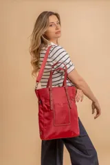 Bolso tote rojo con correa bandolera ajustable y doble asa de mano. Presenta un bolsillo frontal con cierre y detalles de costuras a tono.
