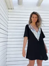 Túnica corta negra con escote en V profundo y apliques de lentejuelas plateadas en el borde del escote.