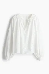 Blusa blanca de algodón con broderie, corte holgado, cuello mao con frunces, abertura en V y mangas globo largas con puños abotonados.