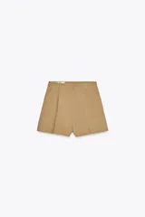 Bermudas color beige de tiro alto con pinzas delanteras, bolsillos laterales y cierre frontal con cremallera y ganchos metálicos.