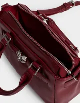 Cartera mini city de cuerina color rojo, con doble asa corta, correa regulable y desmontable, cierre superior y broche metálico de corazón.