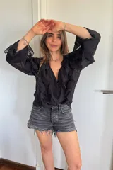 Blusa negra con escote en V, botones frontales y mangas largas con volados.
