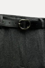 Pantalón negro de tiro alto con pinzas delanteras, pernera ancha y cinturón de cuero con hebilla dorada.