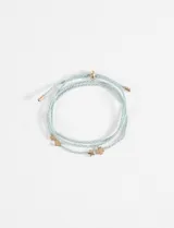 Pulsera de cordón rojo y blanco con dijes metálicos dorados en forma de corazón y tréboles.