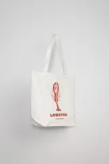 Bolso tipo tote bag de tela color crudo con estampa de una langosta roja y texto "Lobster The Sea Capsule".