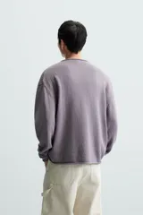 Jersey color crudo de algodón con textura, corte relaxed fit, cuello redondo y manga larga. Acabados en rib con detalle de vuelta.