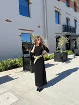Vestido negro de corte midi, con mangas largas ajustadas y cuello redondo. Incluye cinturón ancho con apliques circulares.