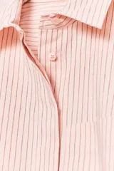 Camisa color rosa claro a rayas verticales finas color marrón, de popelín, con cuello solapa y manga corta con dobladillo. Tiene un bolsillo de parche en el pecho, aberturas laterales en el bajo y pinzas en la espalda. El cierre frontal es con botones ocultos.