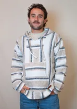 Buzo estilo mexicano con capucha, de tejido grueso a rayas horizontales en tonos blanco, beige y negro. Tiene bolsillo tipo canguro y cordones ajustables en la capucha.