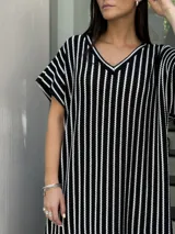 Vestido largo de tejido a rayas horizontales en tonos beige y blanco, con escote en V y mangas cortas tipo murciélago. Presenta tajos laterales en el ruedo.