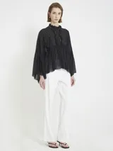 Blusa negra de gasa liviana, con silueta holgada y mangas amplias. Tiene volados frontales, detalles de encaje y cuello alto fruncido, con un estilo romántico y bohemio.