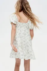 Vestido corto blanco con estampado de flores azules, escote corazón, mangas cortas abullonadas con elástico en hombros y puños, espalda fruncida, corte ajustado en el busto y falda con vuelo y costura fruncida en el bajo.
